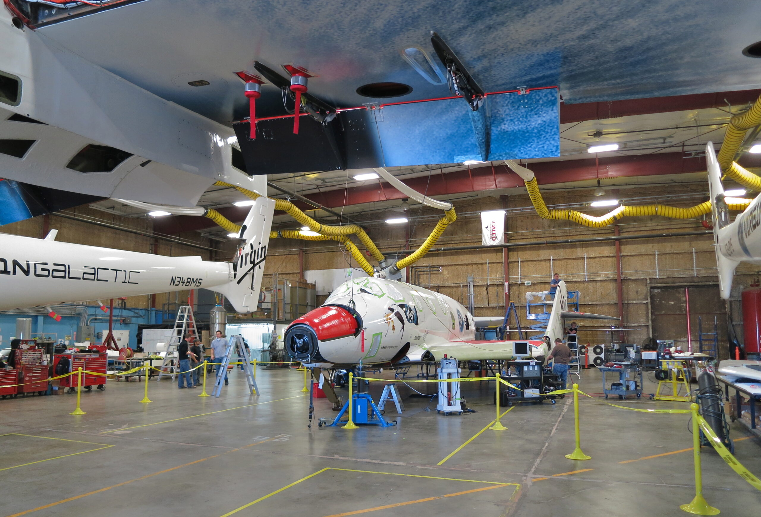 Space Ship Two inside a Mojave hangar with the carrier aircraft overhead